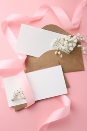 Blank cards, envelopes, ribbon and gypsophila flowers on pink background, flat lay