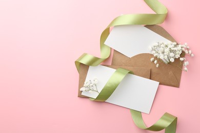 Blank cards, envelopes, ribbon and gypsophila flowers on pink background, flat lay. Space for text