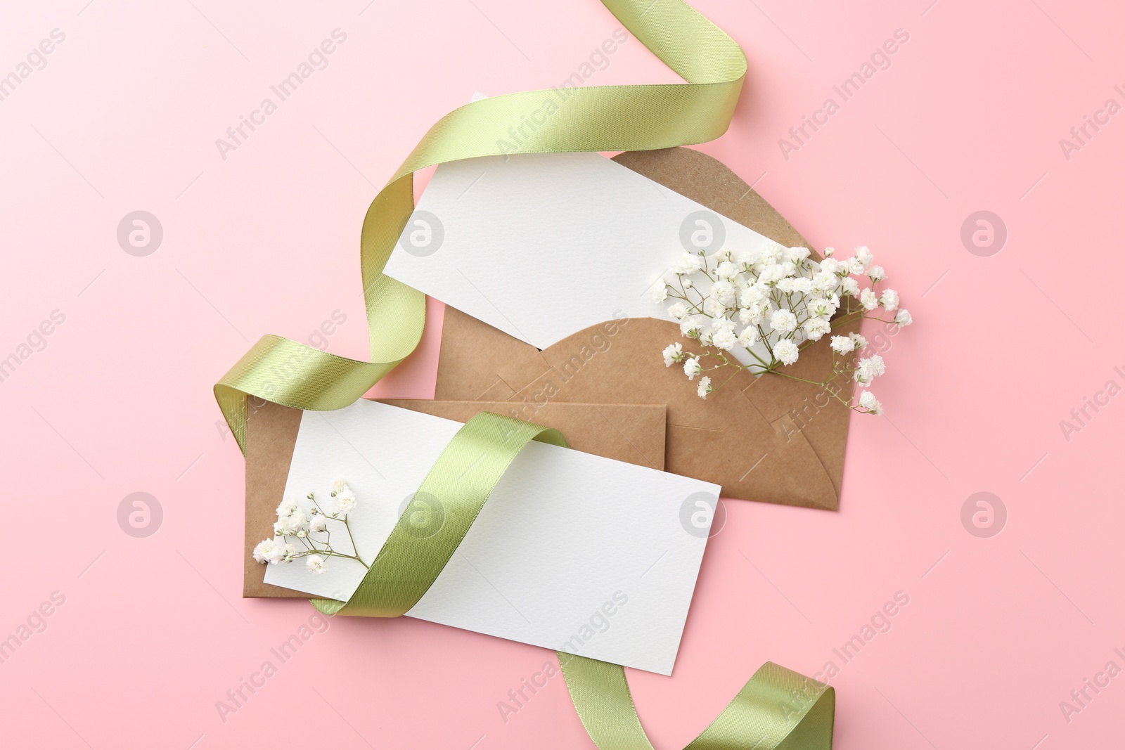 Photo of Blank cards, envelopes, ribbon and gypsophila flowers on pink background, flat lay