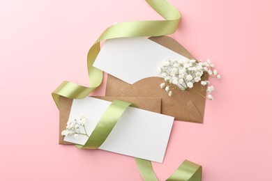 Blank cards, envelopes, ribbon and gypsophila flowers on pink background, flat lay