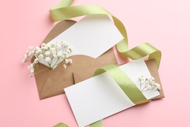 Photo of Blank cards, envelopes, ribbon and gypsophila flowers on pink background, flat lay