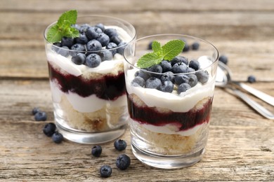 Photo of Tasty trifle dessert. Sponge cake, blueberries, jam and whipped cream in glasses on wooden table, closeup