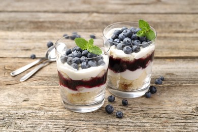 Photo of Tasty trifle dessert. Sponge cake, blueberries, jam and whipped cream in glasses on wooden table, closeup