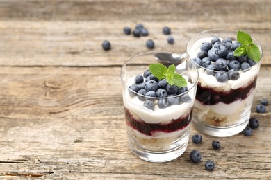 Photo of Tasty trifle dessert. Sponge cake, blueberries, jam and whipped cream in glasses on wooden table, closeup. Space for text