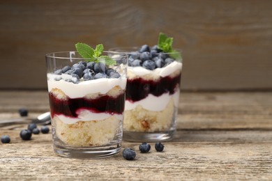 Photo of Tasty trifle dessert. Sponge cake, blueberries, jam and whipped cream in glasses on wooden table, closeup