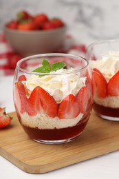 Photo of Tasty trifle dessert. Sponge cake, strawberries, jam and whipped cream in glasses on white table, closeup