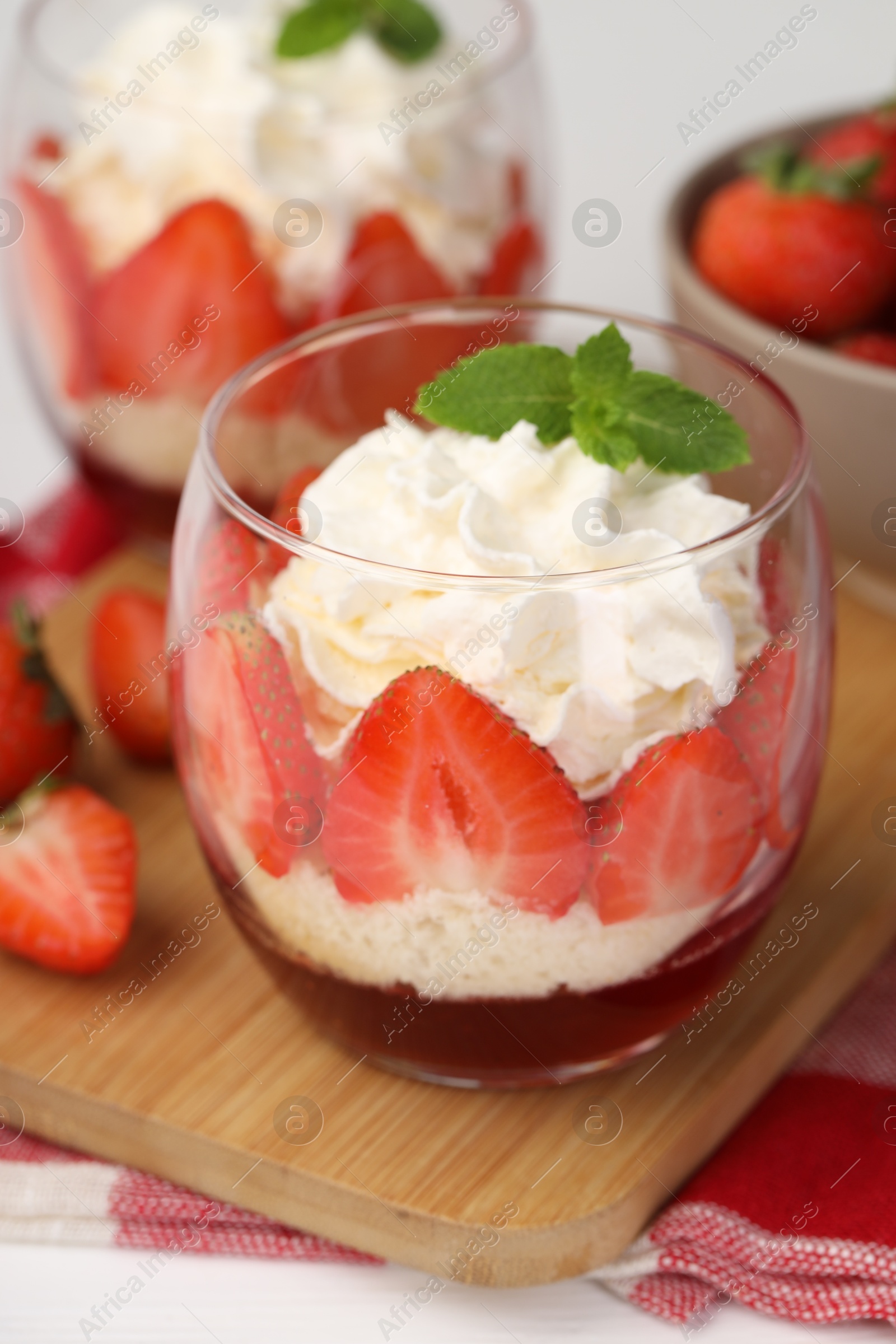 Photo of Tasty trifle dessert. Sponge cake, strawberries, jam and whipped cream in glasses on table, closeup