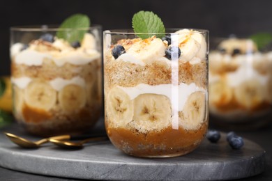 Photo of Tasty trifle dessert. Sponge cake, blueberries, banana and whipped cream in glasses on table, closeup