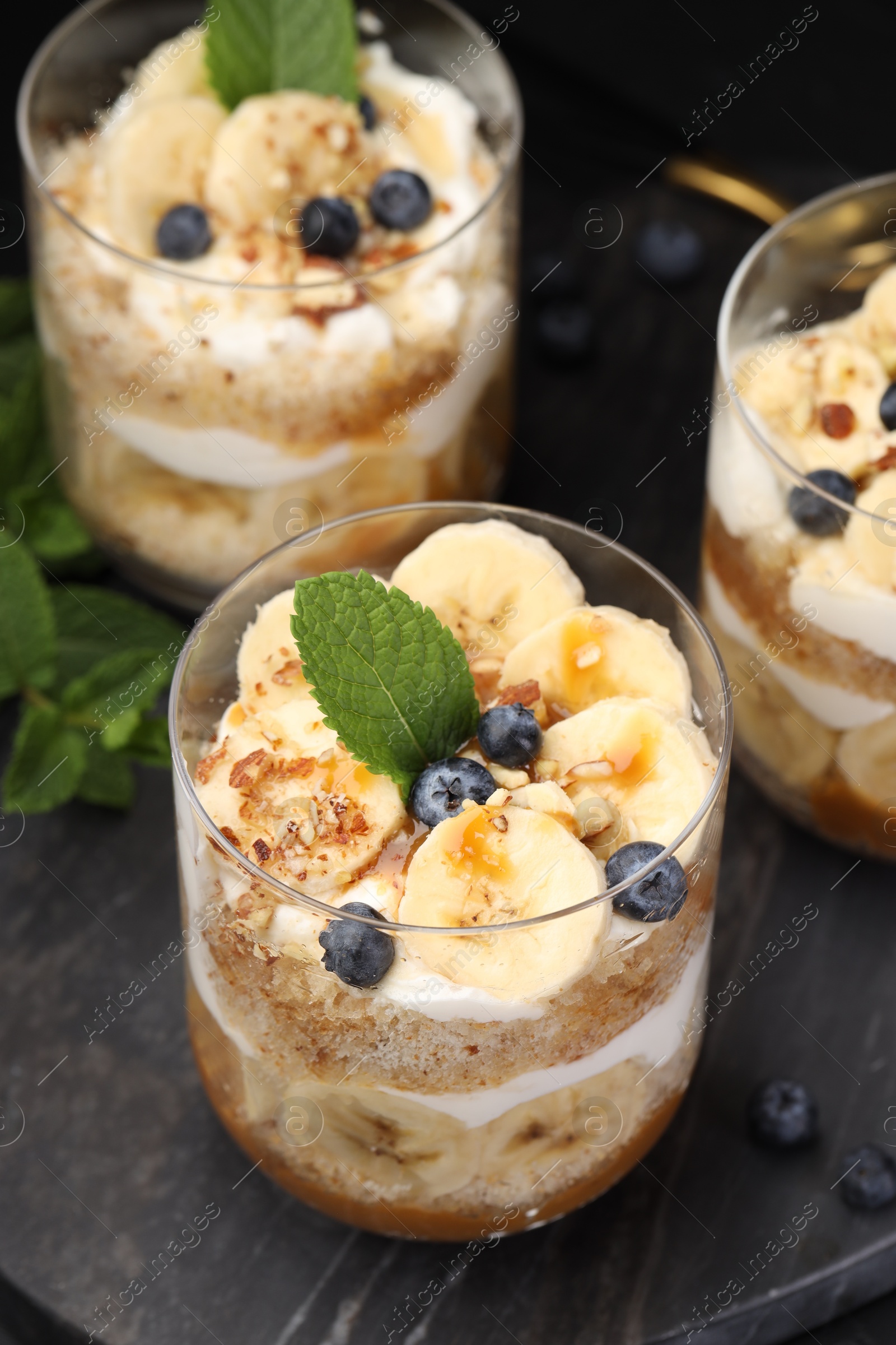 Photo of Tasty trifle dessert. Sponge cake, blueberries, banana and whipped cream in glasses on table, closeup