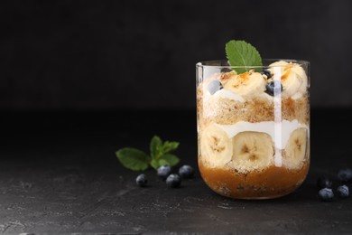 Photo of Tasty trifle dessert. Sponge cake, blueberries, banana and whipped cream in glass on black table, space for text