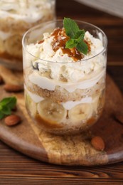 Photo of Tasty trifle dessert. Sponge cake, banana and whipped cream in glass on wooden table, closeup