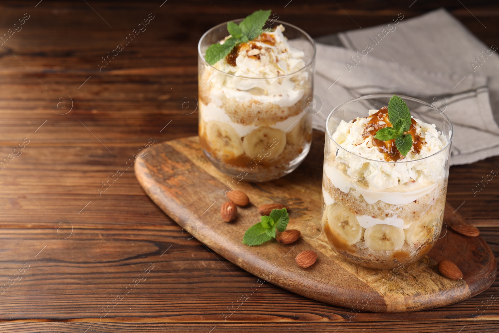 Photo of Tasty trifle dessert. Sponge cake, banana and whipped cream in glasses on wooden table