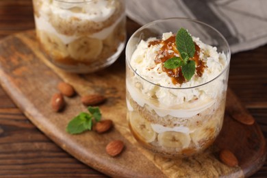 Photo of Tasty trifle dessert. Sponge cake, banana and whipped cream in glasses on wooden table, closeup