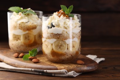 Photo of Tasty trifle dessert. Sponge cake, banana and whipped cream in glasses on wooden table, closeup