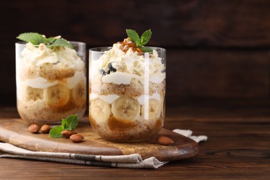 Photo of Tasty trifle dessert. Sponge cake, banana and whipped cream in glasses on wooden table