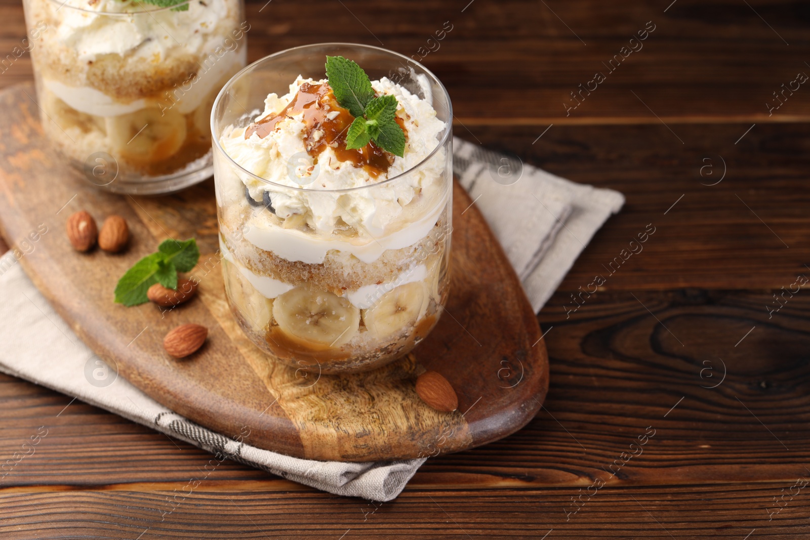 Photo of Tasty trifle dessert. Sponge cake, banana and whipped cream in glasses on wooden table, closeup