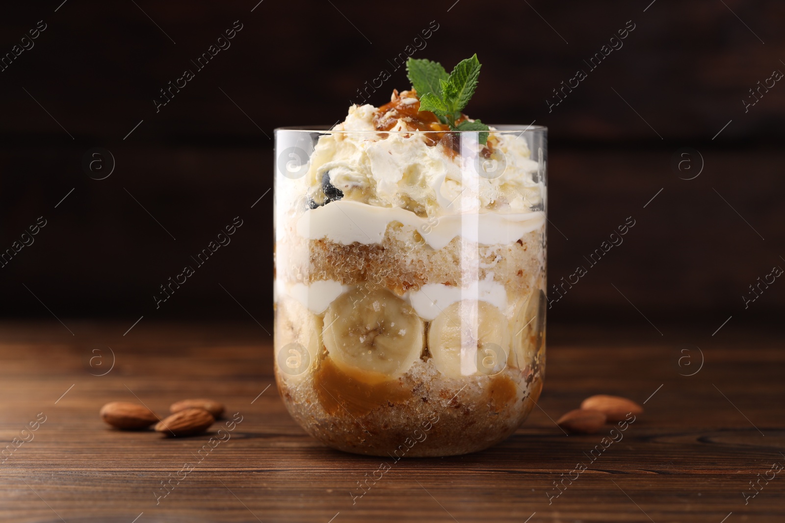 Photo of Tasty trifle dessert. Sponge cake, banana and whipped cream in glass on wooden table, closeup