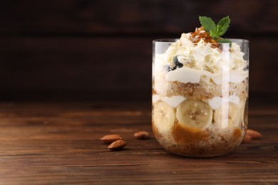 Tasty trifle dessert. Sponge cake, banana and whipped cream in glass on wooden table, closeup. Space for text