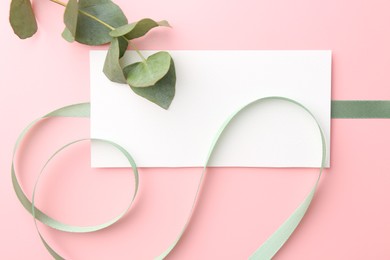 Blank card, ribbon and eucalyptus branch on pink background, flat lay