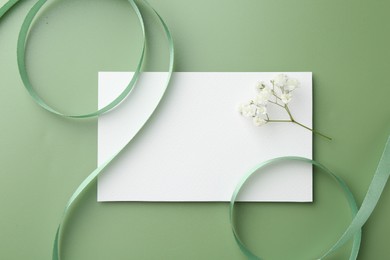 Blank card, ribbons and gypsophila flowers on green background, flat lay