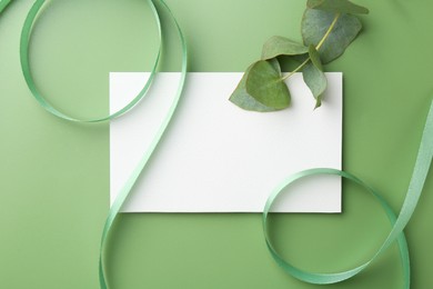 Blank card, ribbons and eucalyptus branch on green background, flat lay