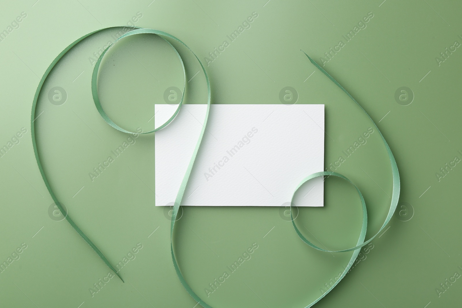 Photo of Blank card and ribbon on green background, top view