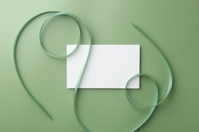 Blank card and ribbon on green background, top view