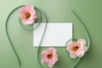 Blank card, ribbons and eustoma flowers on green background, flat lay