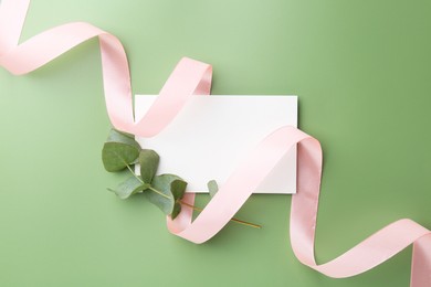 Blank card, ribbon and eucalyptus branch on green background, top view