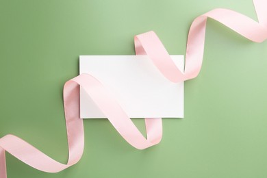 Blank card and ribbon on green background, top view