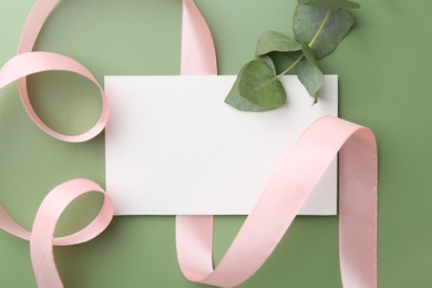 Blank card, ribbon and eucalyptus branch on green background, flat lay