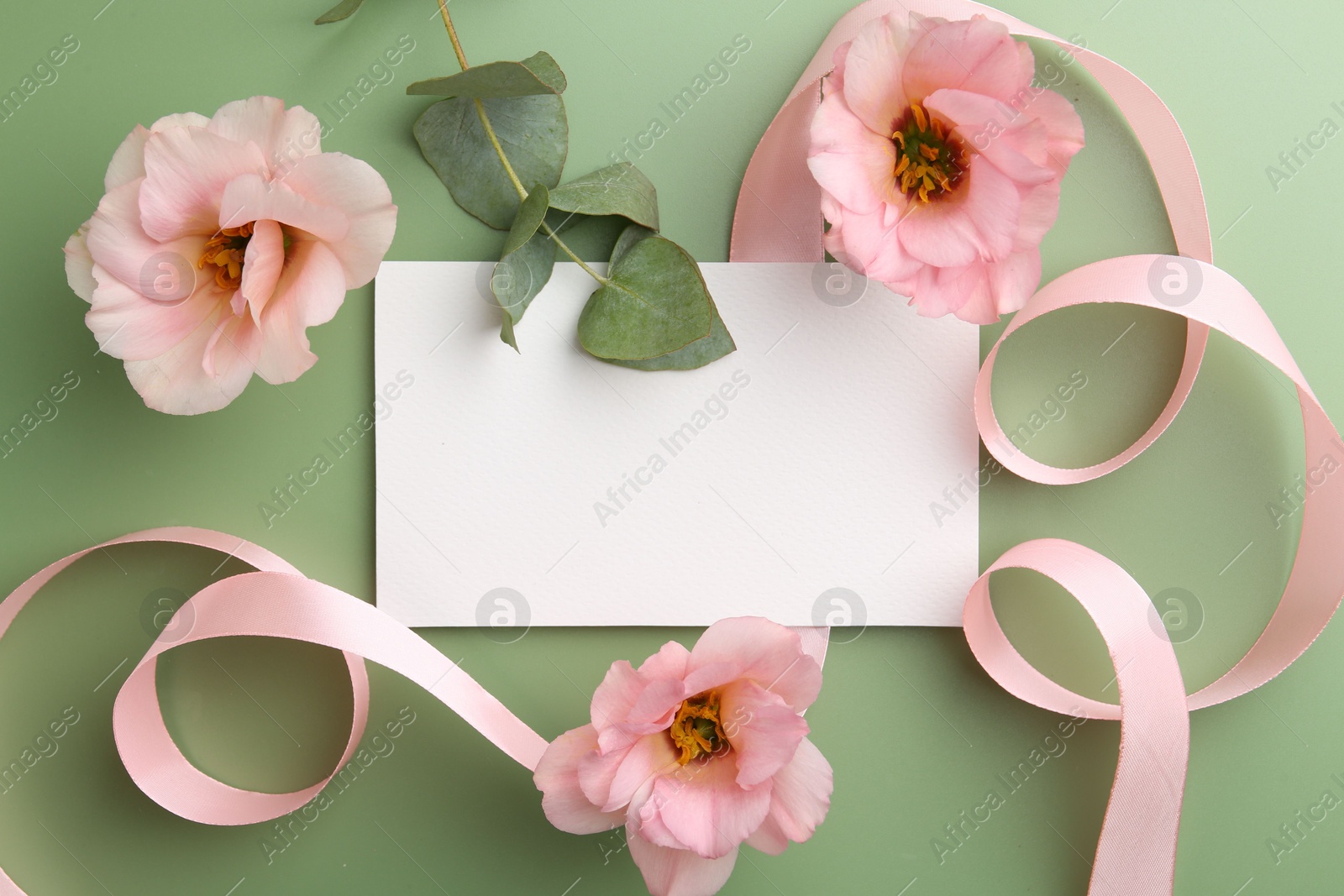 Photo of Blank card, ribbon, eustoma flowers and eucalyptus branch on green background, flat lay