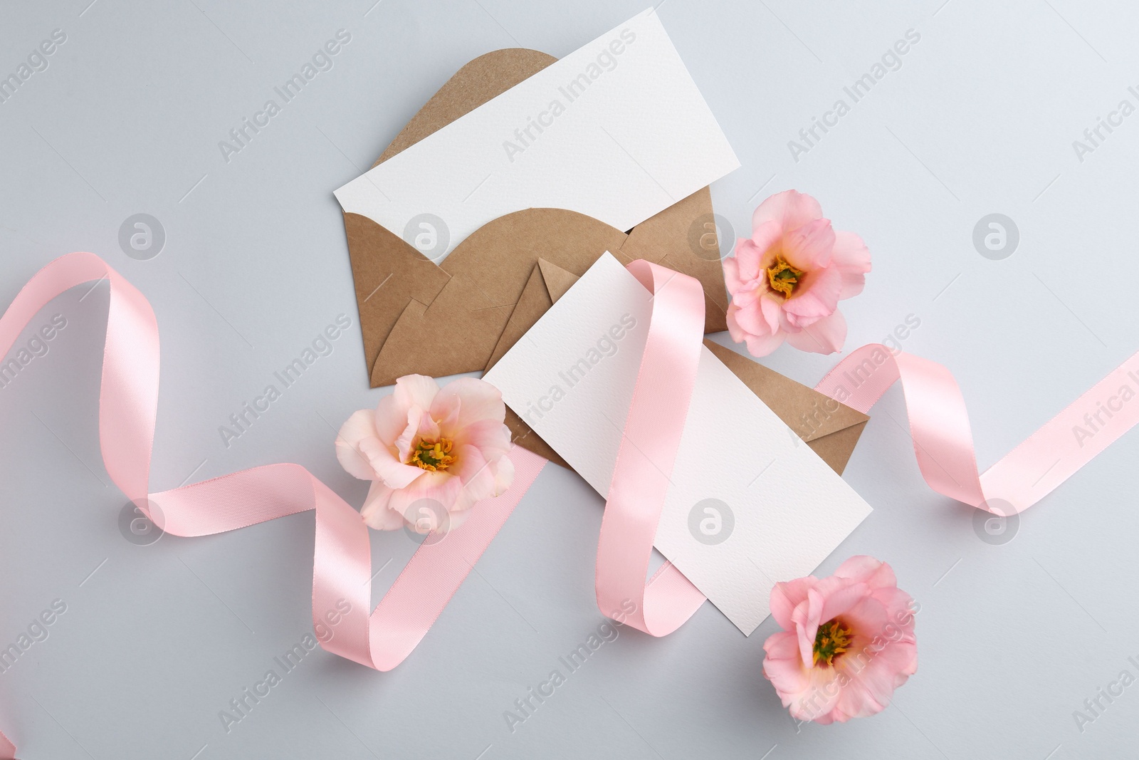 Photo of Flat lay composition with blank cards, ribbon and flowers on light gray background