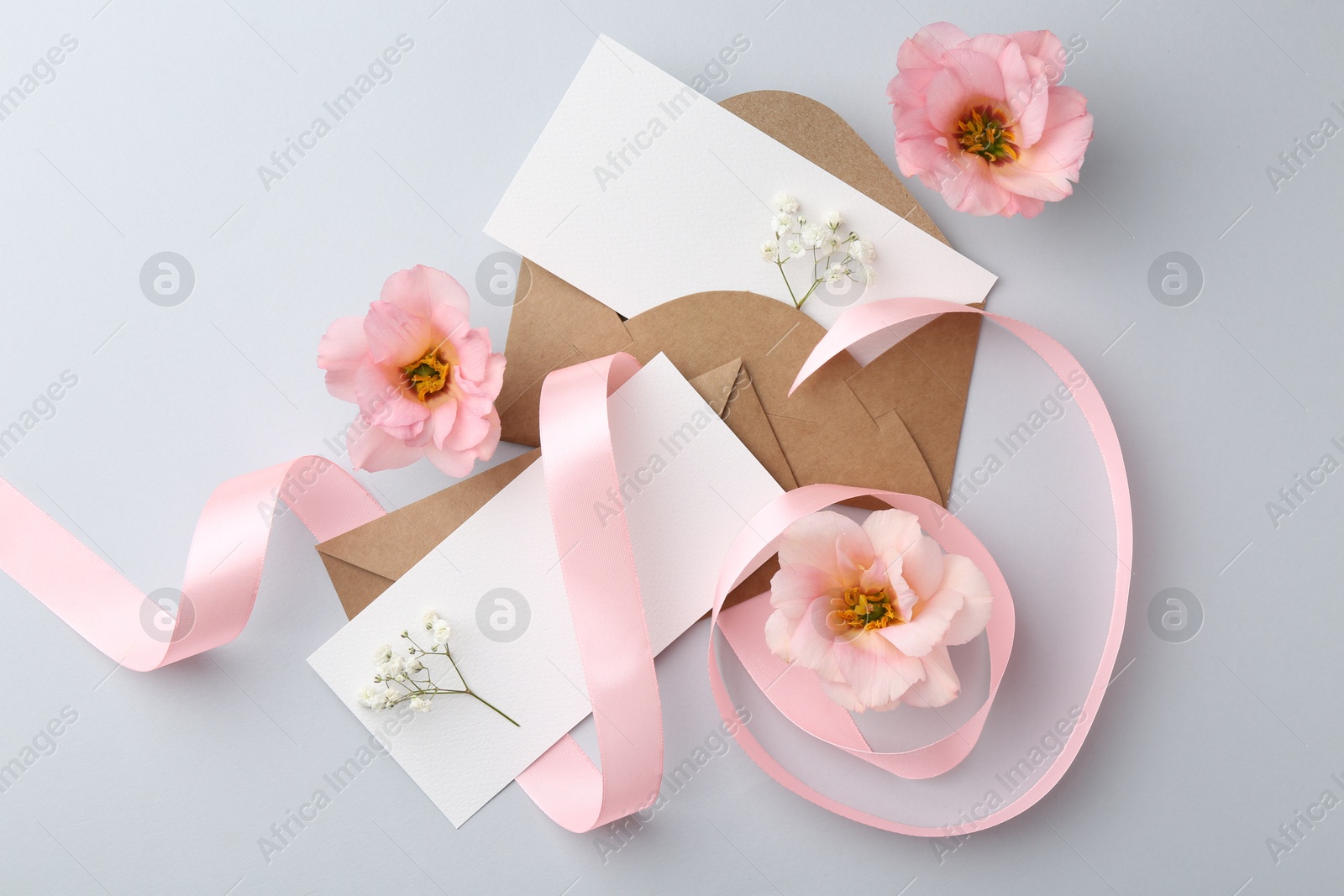 Photo of Flat lay composition with blank cards, ribbon and flowers on light gray background