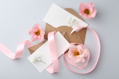 Flat lay composition with blank cards, ribbon and flowers on light gray background