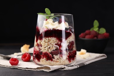 Photo of Tasty trifle dessert. Berries, sponge cake and whipped cream in glass on black wooden table