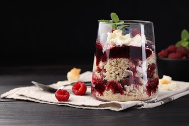 Photo of Tasty trifle dessert. Berries, sponge cake and whipped cream in glass on black wooden table, space for text