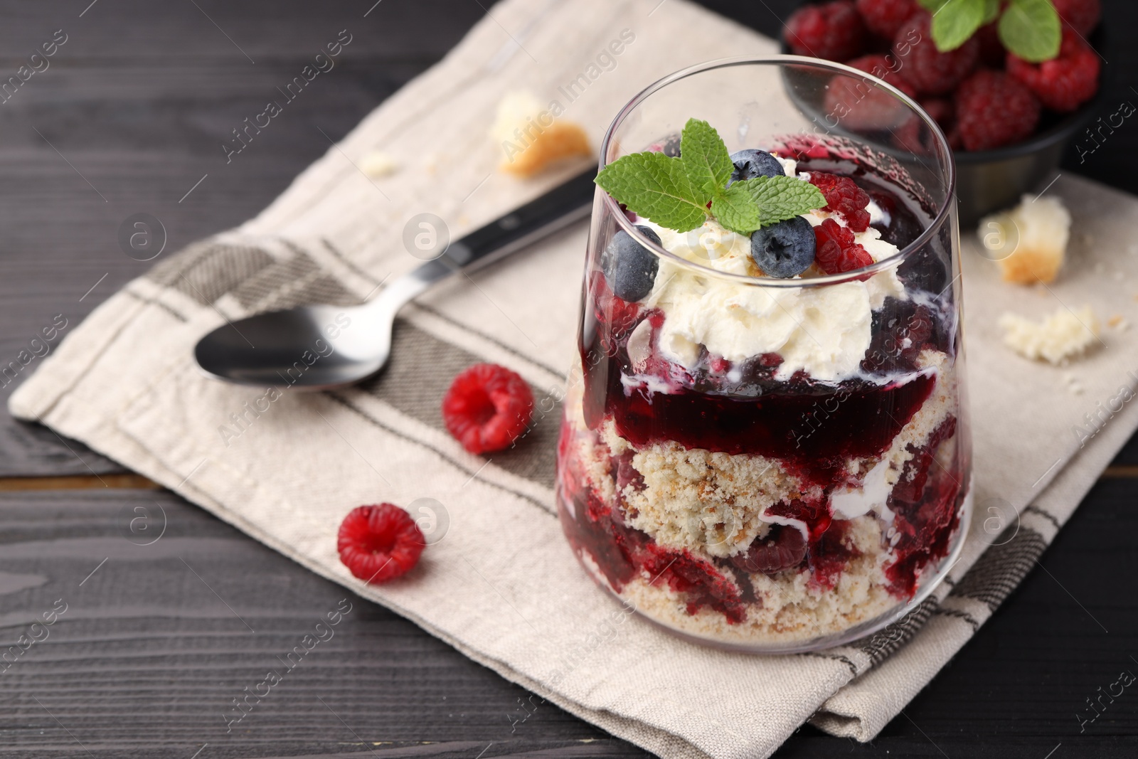 Photo of Tasty trifle dessert. Berries, sponge cake and whipped cream in glass on black wooden table