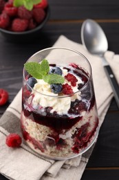 Photo of Tasty trifle dessert. Berries, sponge cake and whipped cream in glass on black wooden table