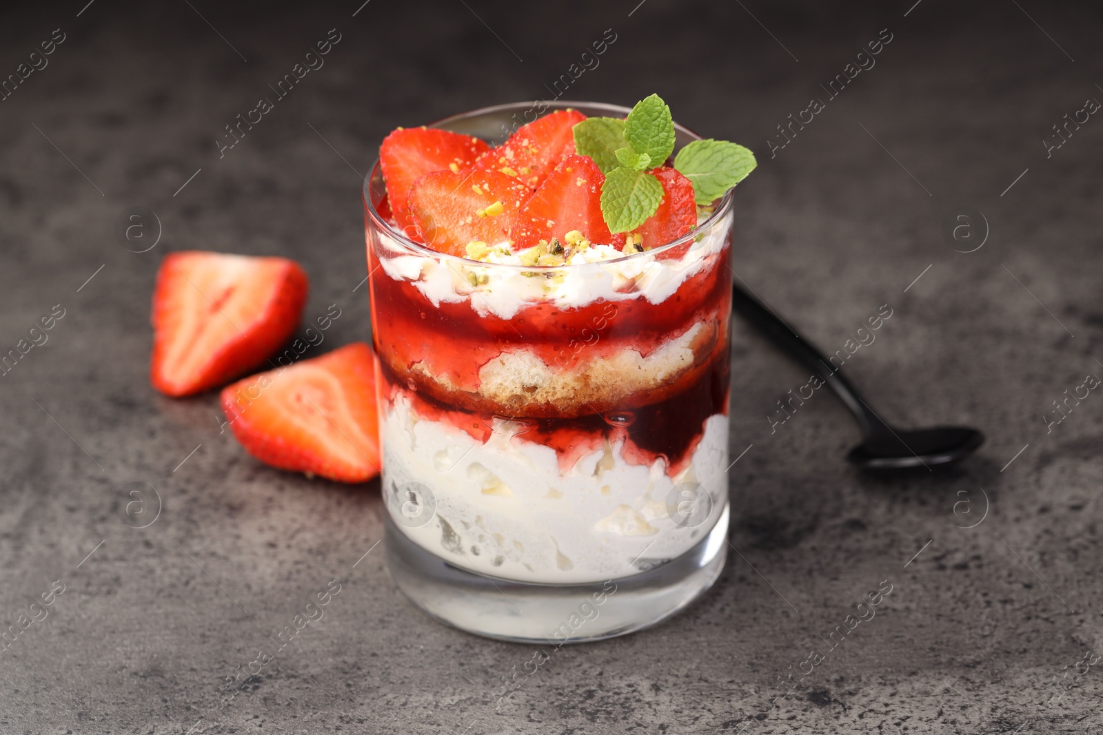 Photo of Tasty trifle dessert. Strawberries, sponge cake and whipped cream in glass on grey table