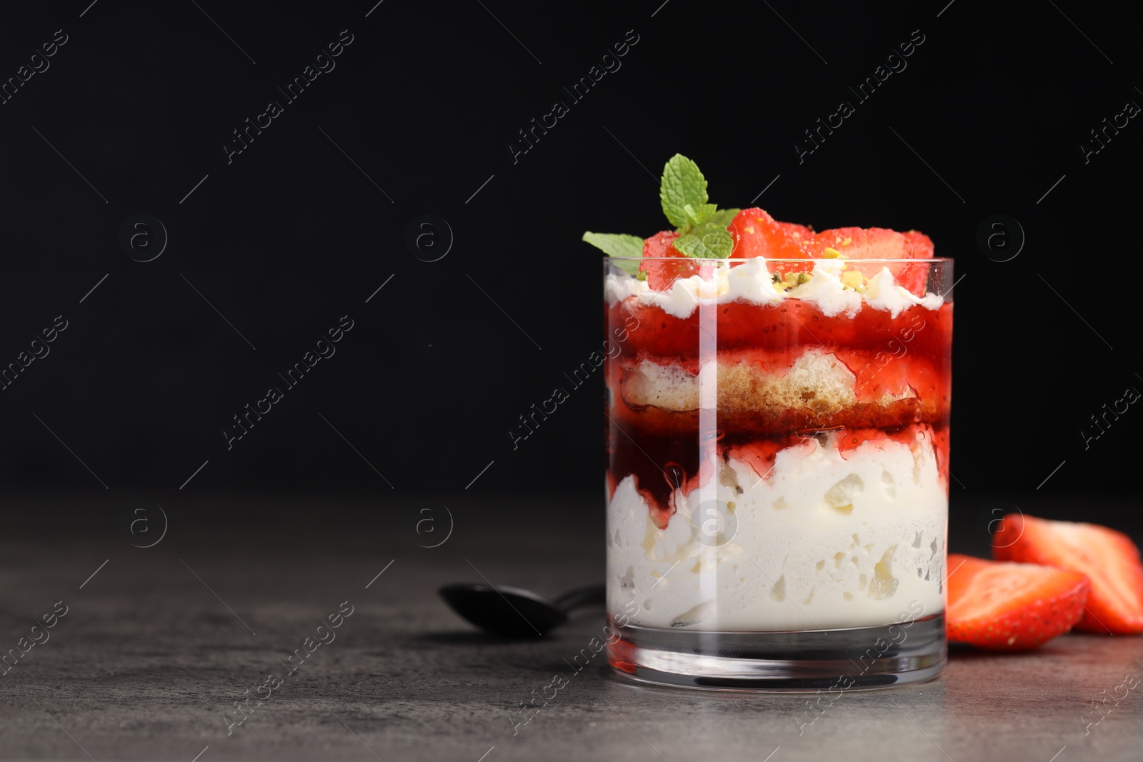 Photo of Tasty trifle dessert. Strawberries, sponge cake and whipped cream in glass on grey table, space for text