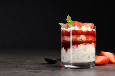 Photo of Tasty trifle dessert. Strawberries, sponge cake and whipped cream in glass on grey table, space for text