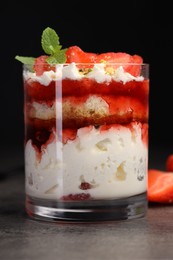 Photo of Tasty trifle dessert. Strawberries, sponge cake and whipped cream in glass on grey table