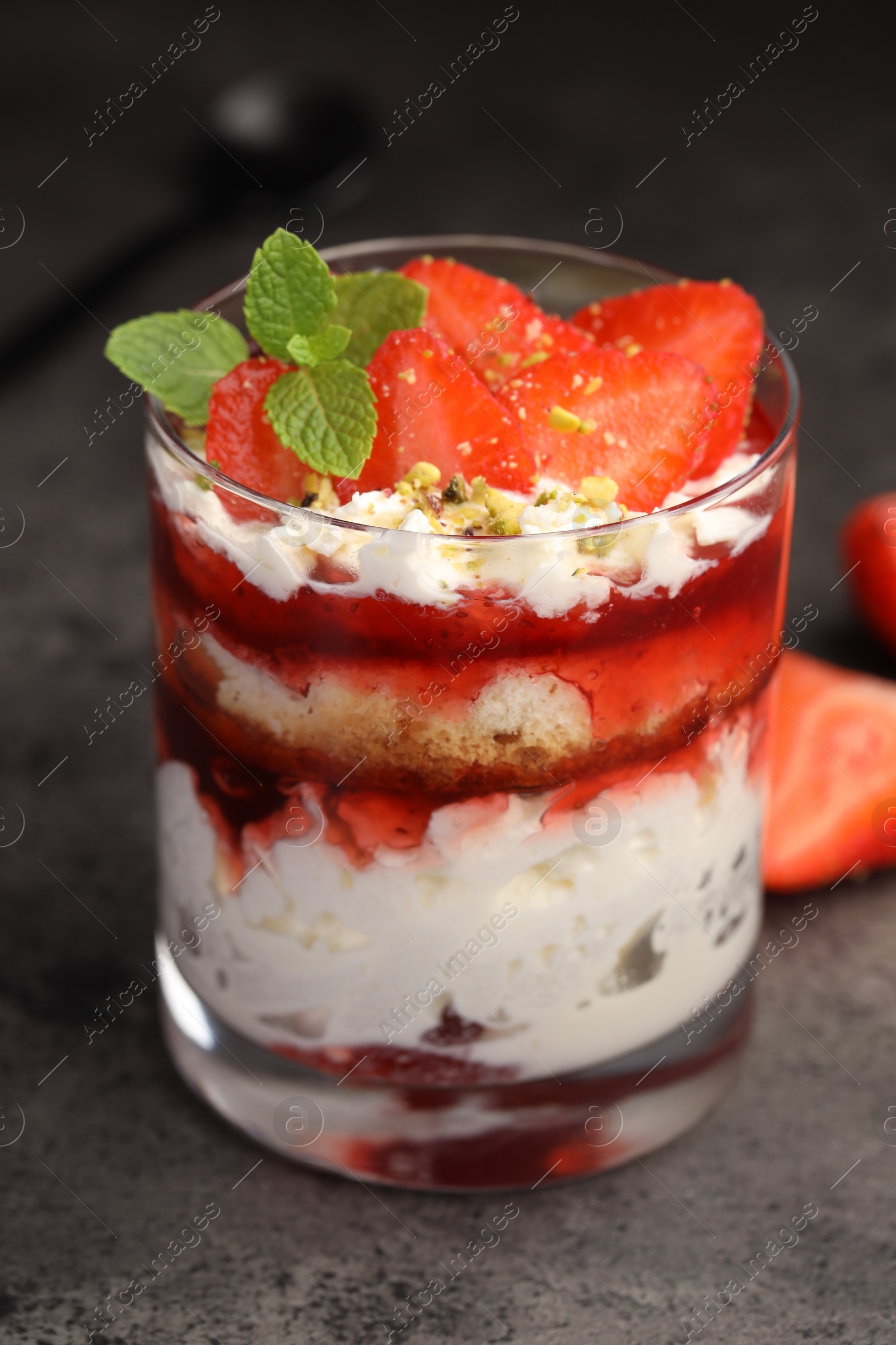 Photo of Tasty trifle dessert. Strawberries, sponge cake and whipped cream in glass on grey table