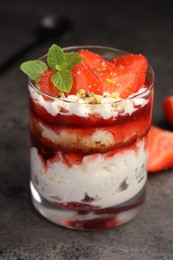 Photo of Tasty trifle dessert. Strawberries, sponge cake and whipped cream in glass on grey table