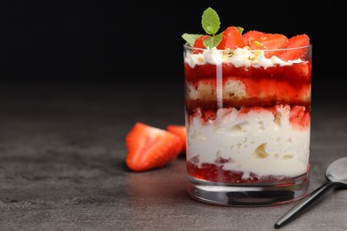 Photo of Tasty trifle dessert. Strawberries, sponge cake and whipped cream in glass on grey table, space for text