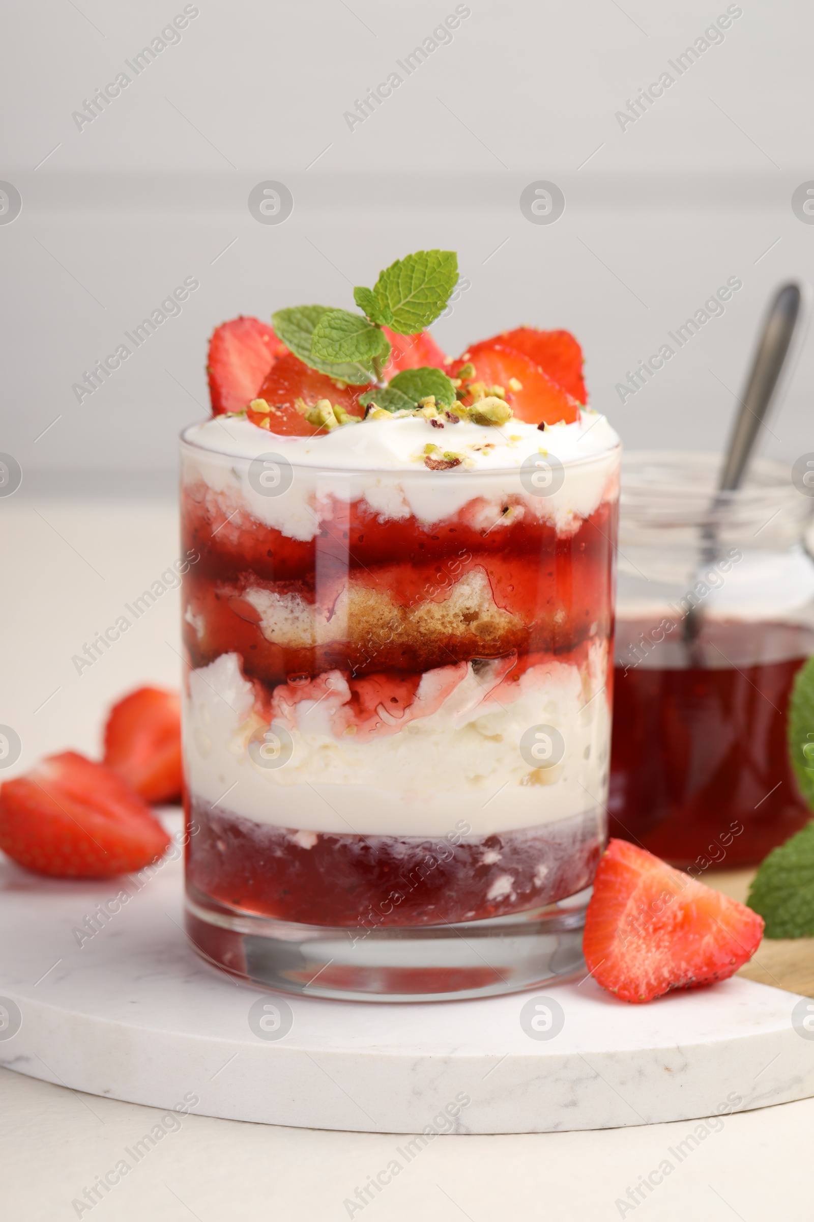 Photo of Tasty trifle dessert. Strawberries, sponge cake and whipped cream in glass on beige table