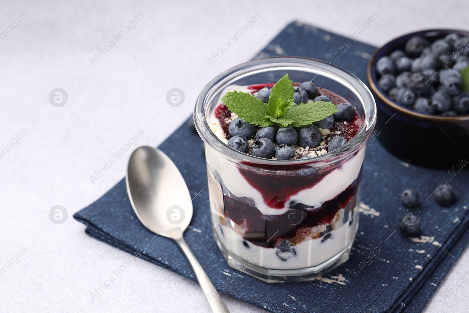 Photo of Tasty trifle dessert. Blueberries, sponge cake and whipped cream in glass on light grey table