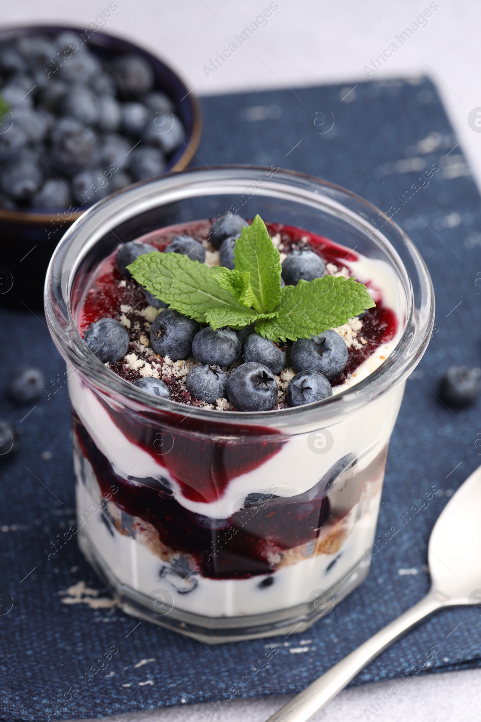 Photo of Tasty trifle dessert. Blueberries, sponge cake and whipped cream in glass on light grey table