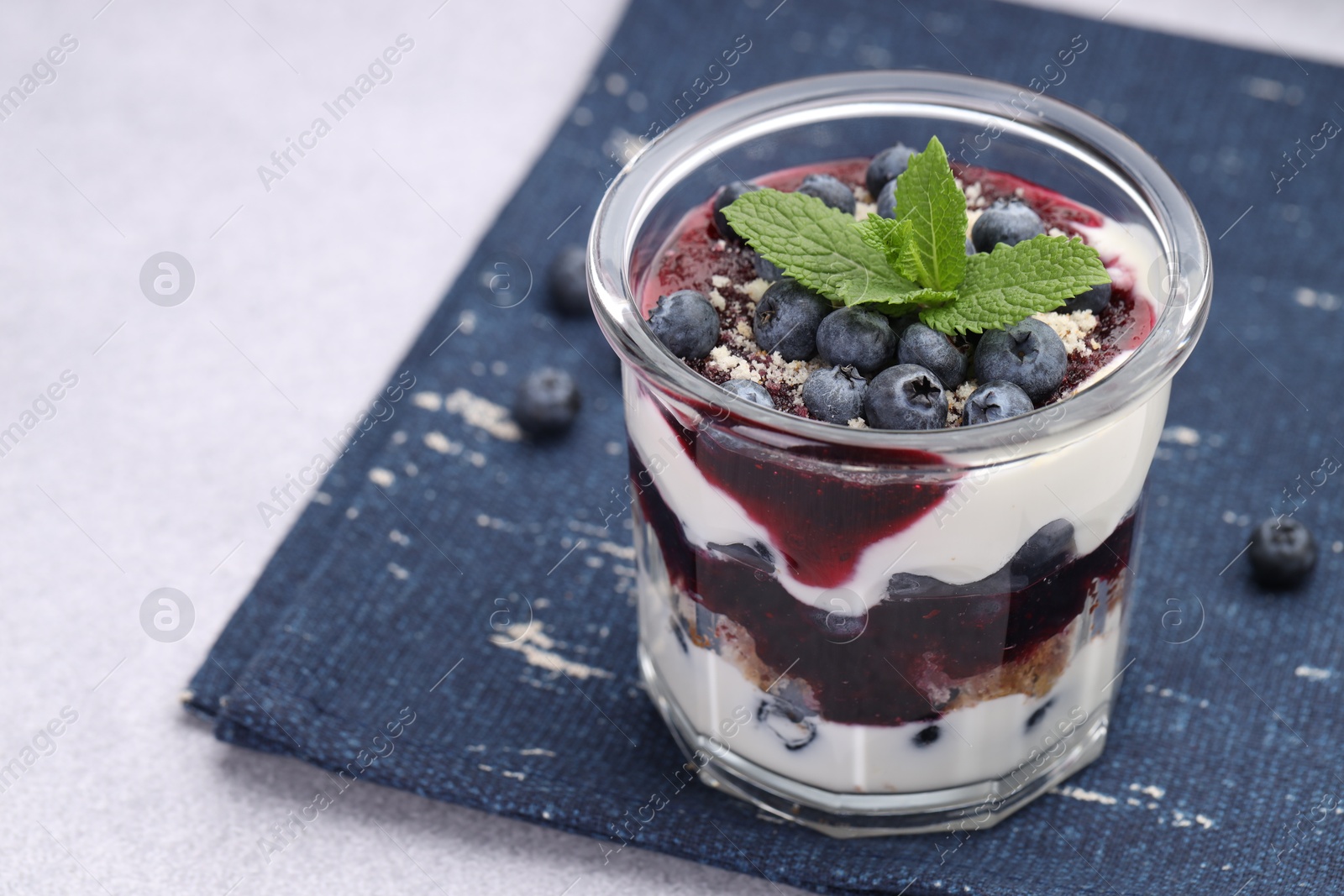 Photo of Tasty trifle dessert. Blueberries, sponge cake and whipped cream in glass on light grey table, space for text